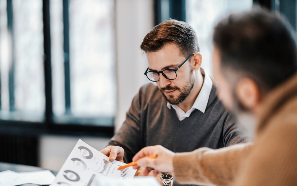 Two Colleagues Are Sitting At The Meeting Room And Discussing Charts And Statistics